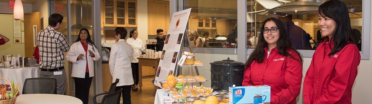 students stand by a cart and hand out food to people 