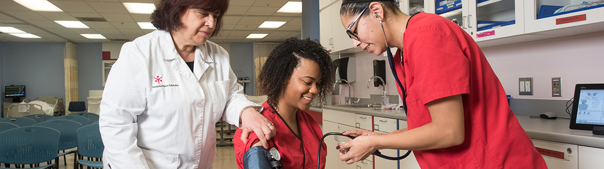 A teacher helps her student take blood pressure of another student 
