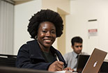 A student looking up from their laptop and smiling to the camera.