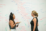 Students talking in front of white board.