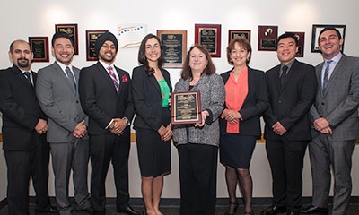 Students smiling with an award behind more awards on the wall.